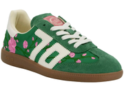 A green suede sneaker featuring a white serrated-style side stripe, white laces, a pink heart-shaped tongue label, and pink floral embroidery with green stems along the side. It has a brown gum sole.