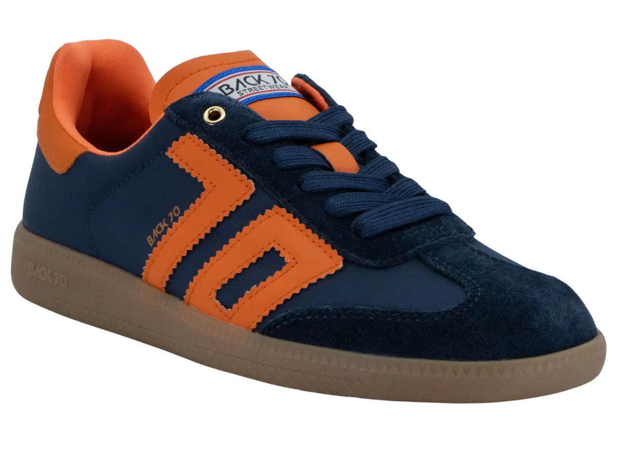 A low-top sneaker by Back 90, featuring navy blue suede and mesh panels with bright orange overlays, matching orange lining, navy laces, and a tan gum sole.