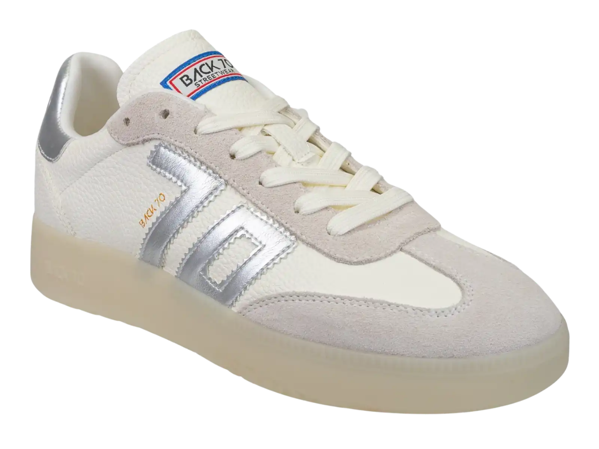 A low-top sneaker by Backshot, featuring a white and light beige suede and leather upper with metallic silver side stripes, a cream-colored sole, and a Backshot logo on the tongue.