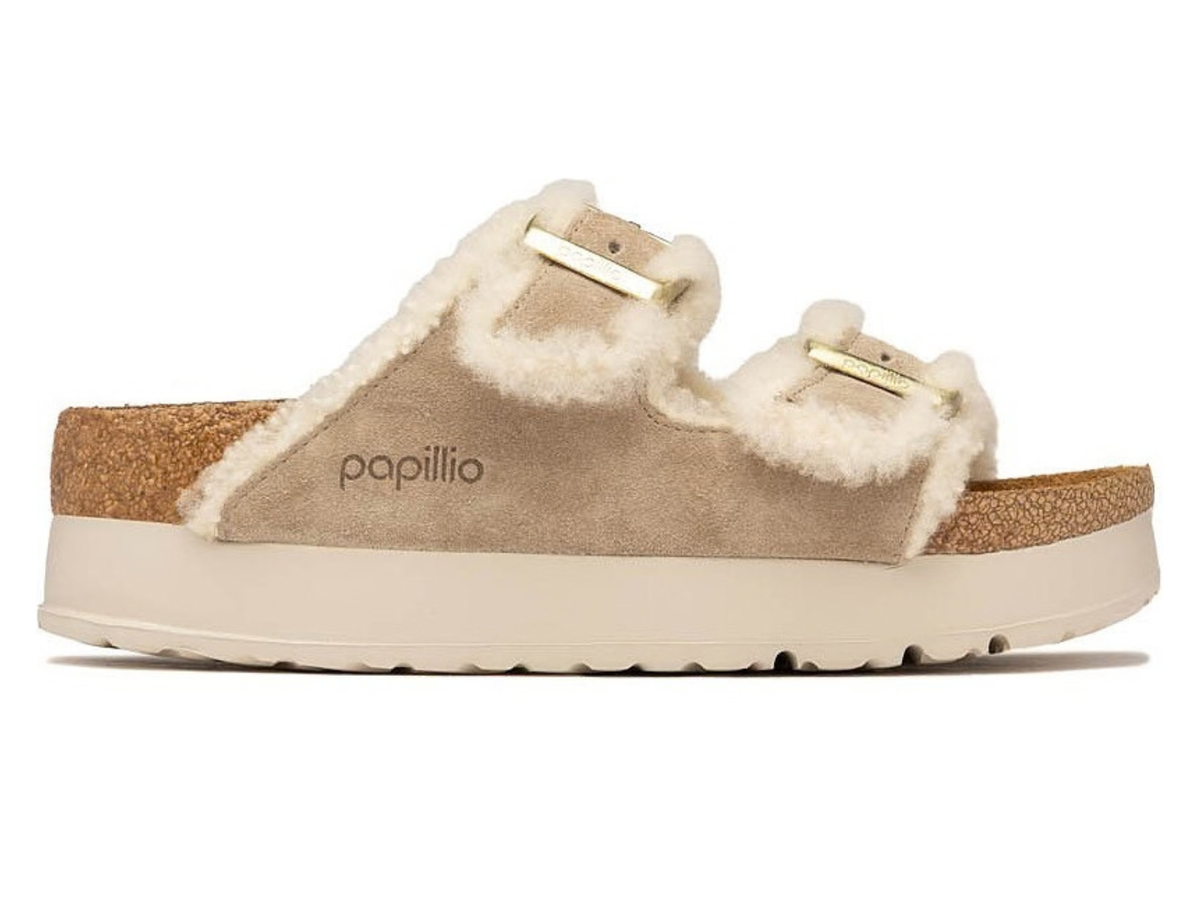 A single Papillio mule slide sandal featuring a beige suede upper, plush cream shearling lining, and gold-tone buckle straps, shown in profile against a white background.