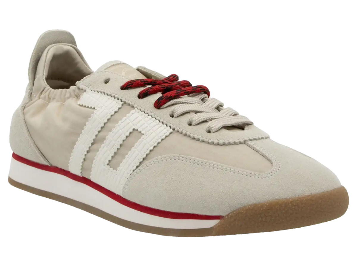 A low-top sneaker in light beige suede and canvas with white side stripes, red laces, a red midsole stripe, and a gum brown outsole, shown on a white background.