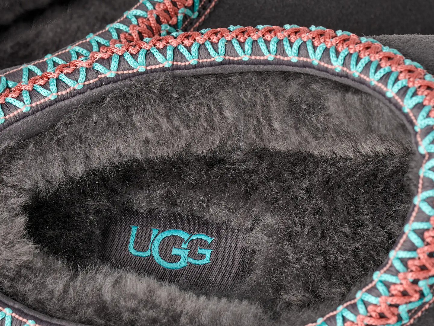 Close-up of UGG brand logo on gray fleece lining with colorful trim.