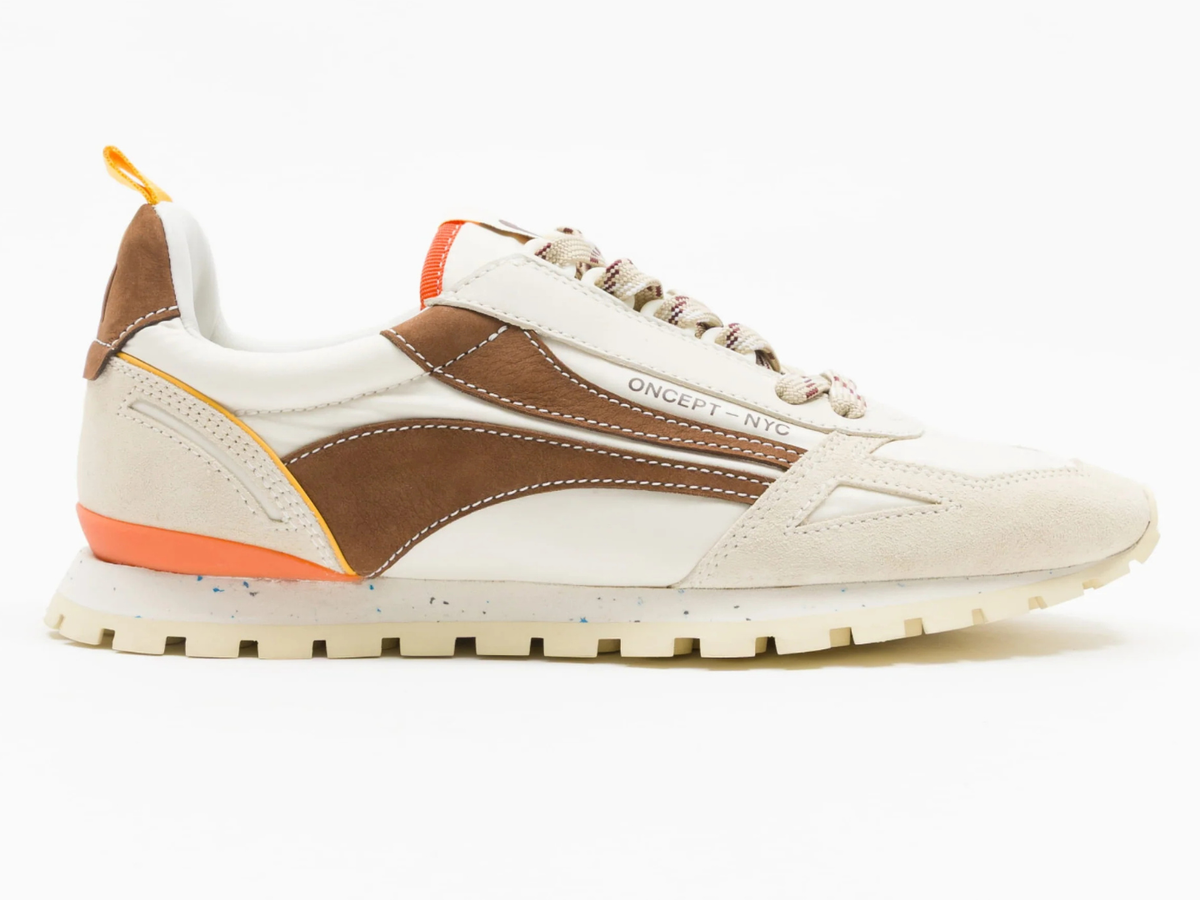 A low-top sneaker in off-white and brown suede, featuring orange accents on the heel and tongue, with 'ONCEPT NYC' printed on the side, set against a plain white background.