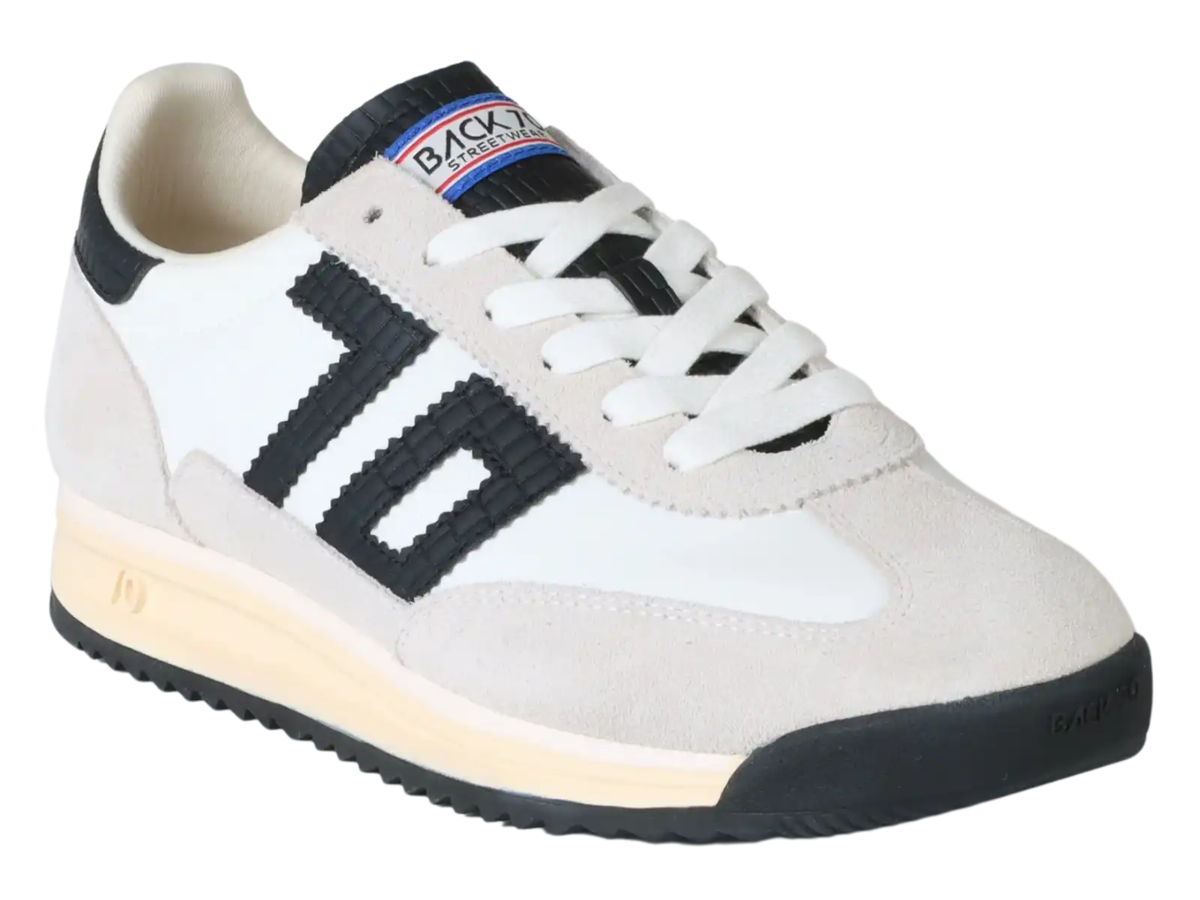 A low-top sneaker with a white and light beige suede upper, featuring a prominent black three-stripe design on the side, white laces, and a black and beige sole.
