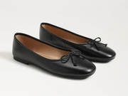 A pair of black leather ballet flats with small bow details on the toes, displayed on a clean white background.
