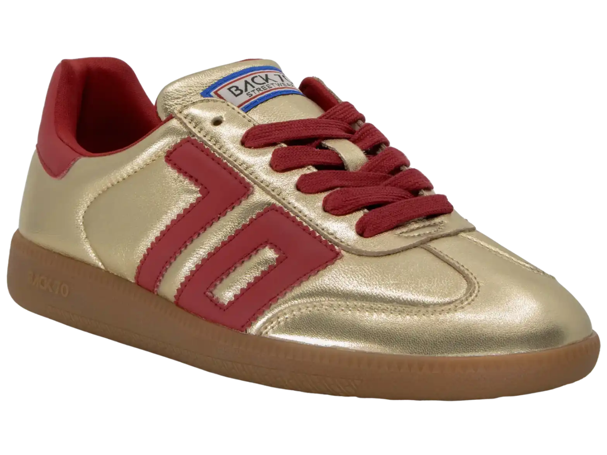 A metallic gold low-top sneaker with red accents, including the side stripes, laces, and heel tab, on a white background.