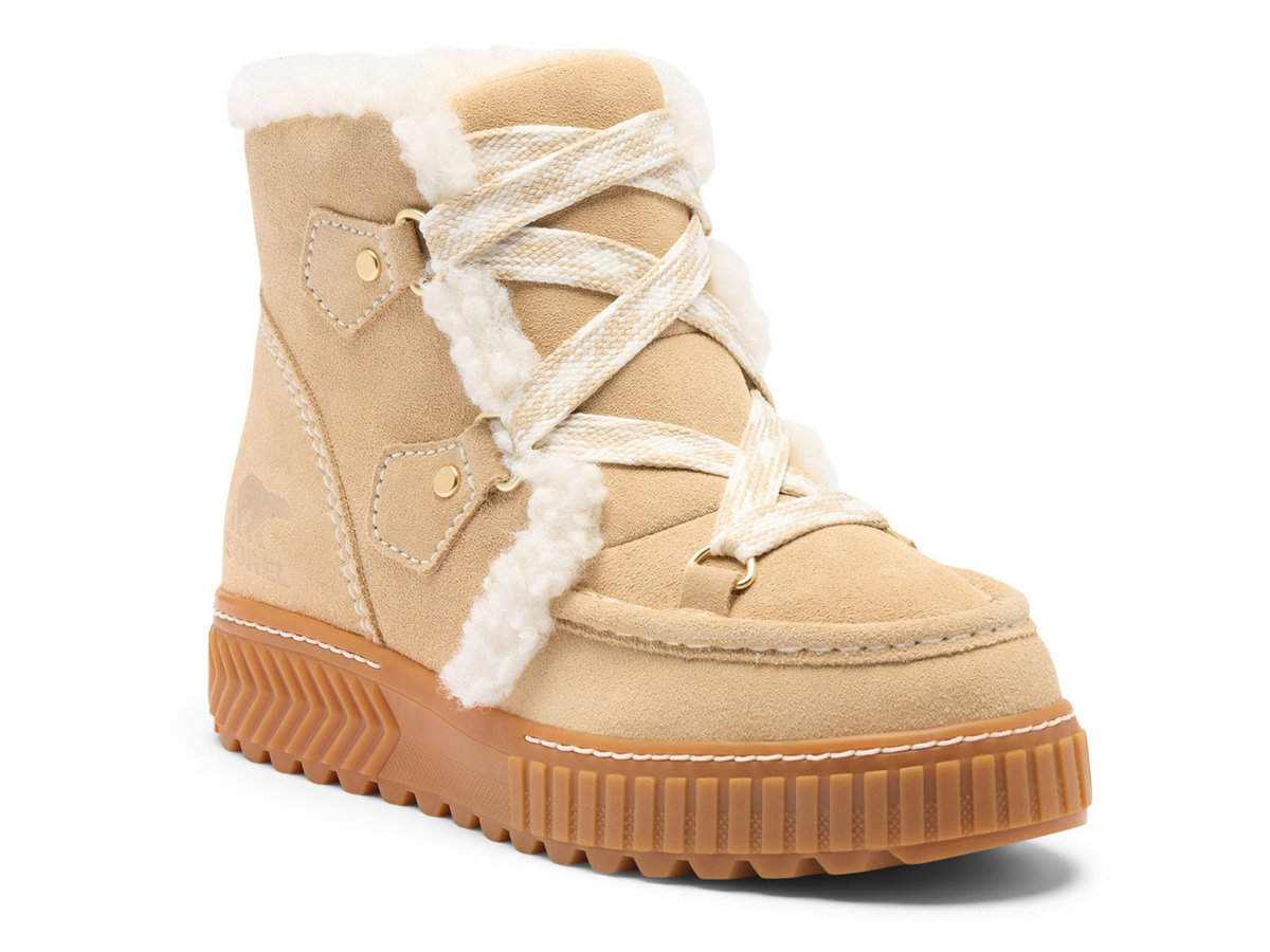 A beige suede ankle boot with white faux-fur trim, cream lace-up detailing, and a chunky brown lug sole, shown on a white background.
