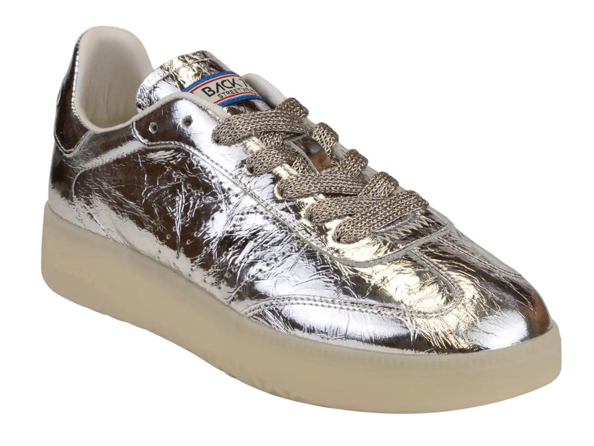 A metallic silver sneaker with a textured, crinkled finish, featuring brownish-beige laces and a thick beige sole, shown against a plain white background.